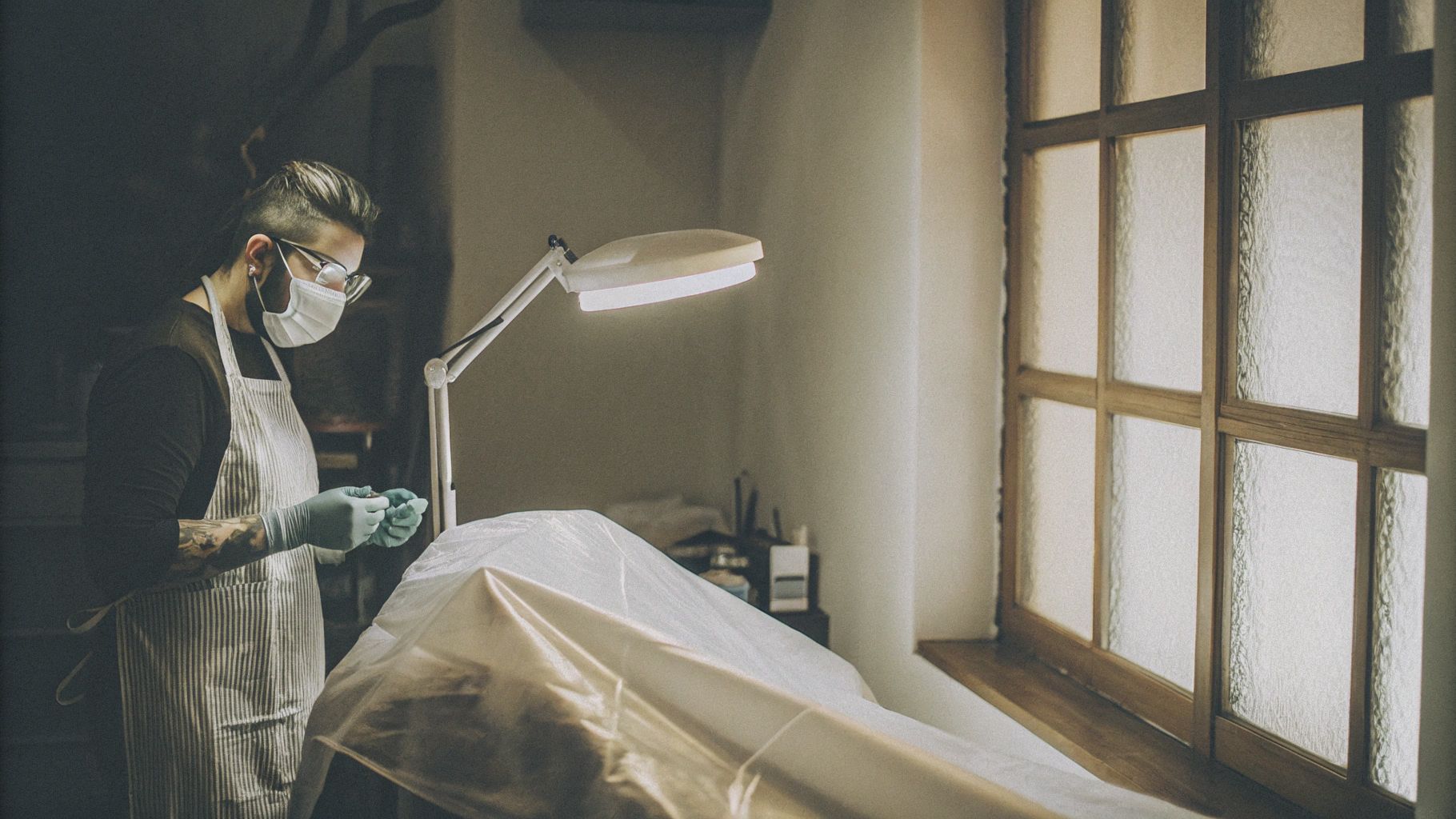 Tattoo artist wearing full PPE, including gloves, apron, mask, and glasses, for bloodborne pathogen protection