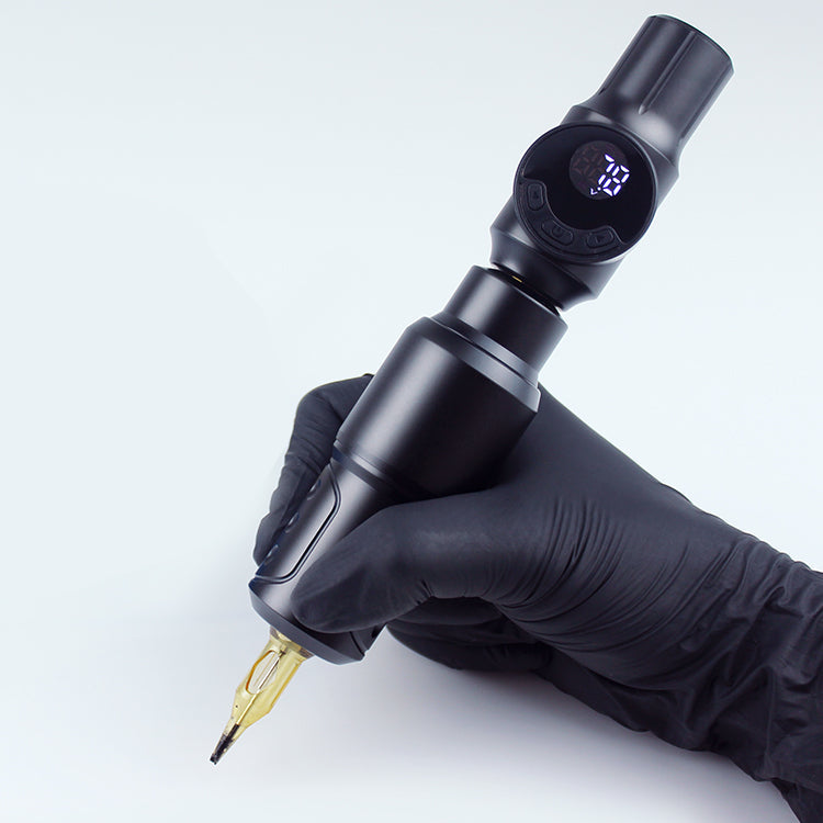 Black wireless tattoo machine pen with digital display, held by artist with black glove, professional tattoo equipment