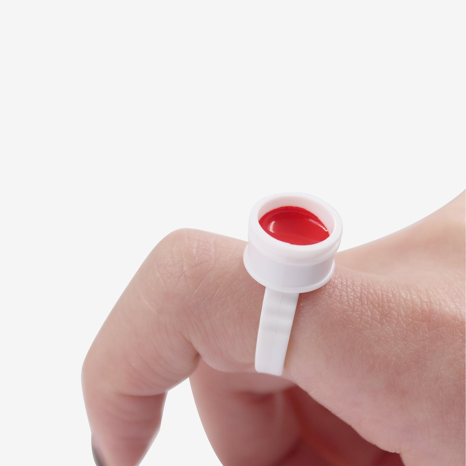 White plastic permanent makeup ink finger ring holding red tattoo pigment for professional PMU use.