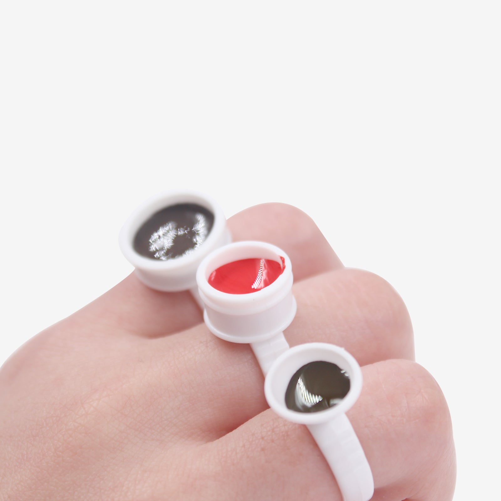 Permanent makeup ink finger ring holding black, red, and dark green pigment. Ideal for tattoo supplies and professional use.