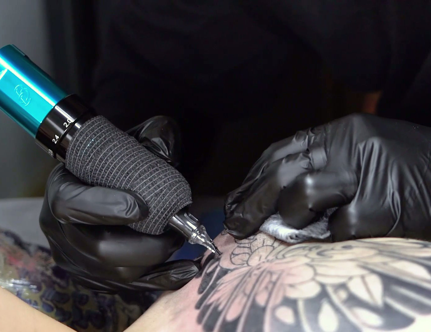 A tattoo artist, wearing black gloves, carefully applies a tattoo to a client's skin. 